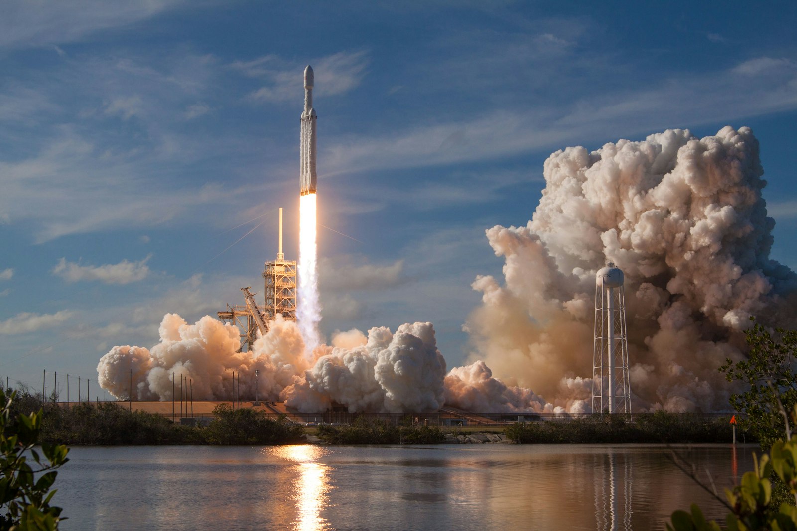 A heavy-lift rocket launch reflected over water.